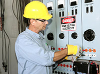 man in PPE standing in front of an electrical panel, which has a hazard warning sign posted on it